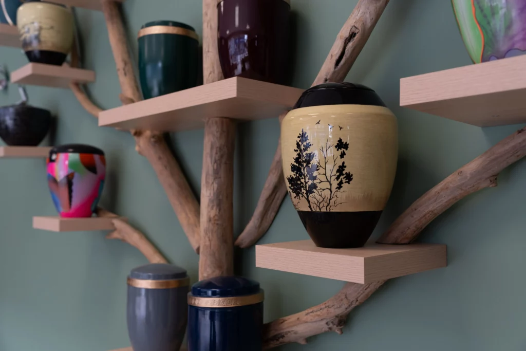 Collection d'urnes funéraires artisanales exposées sur un étagère en bois de flotté.