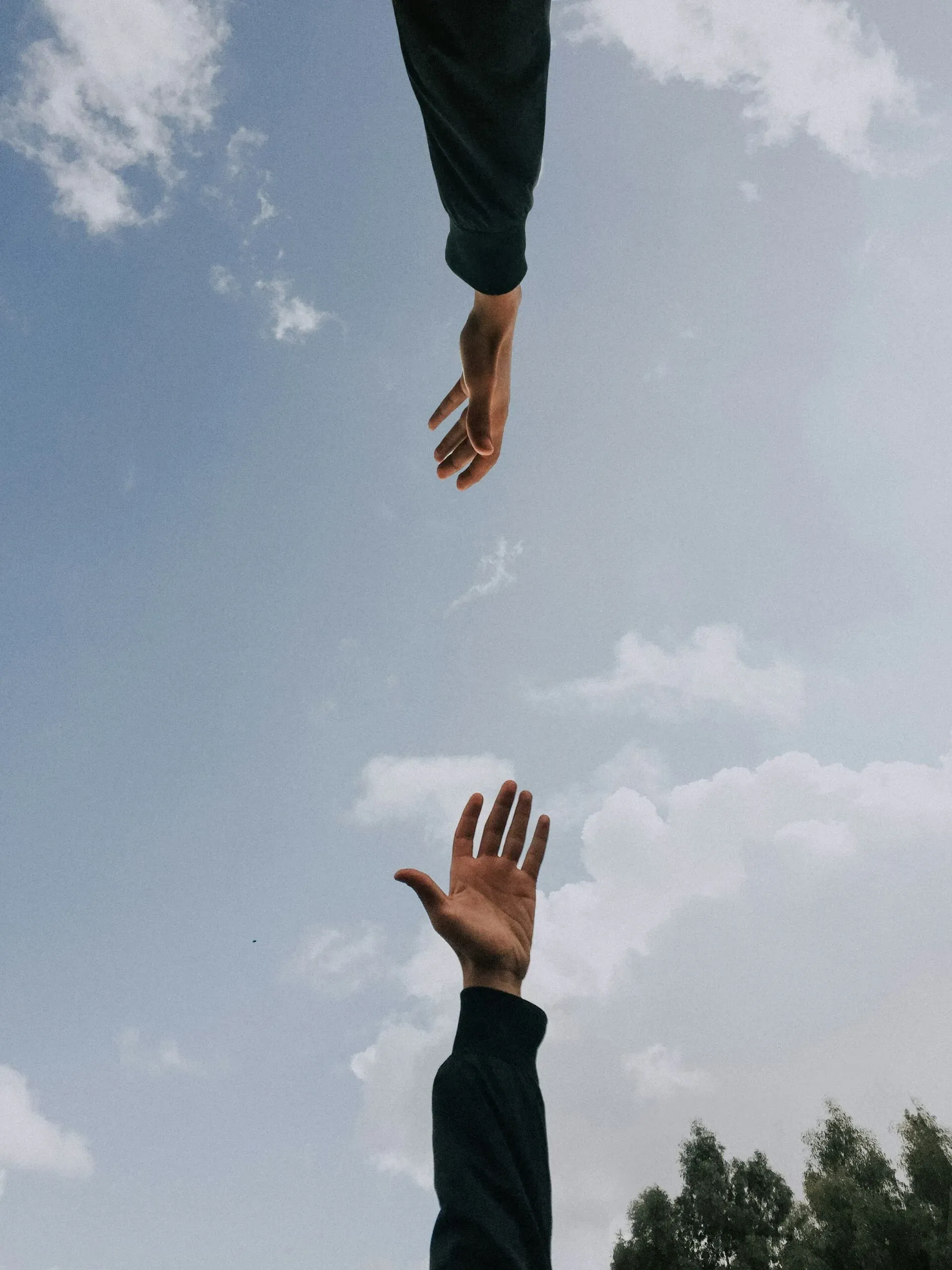 Deux mains tendues l'une vers l'autre sur un fond de ciel bleu nuageux.